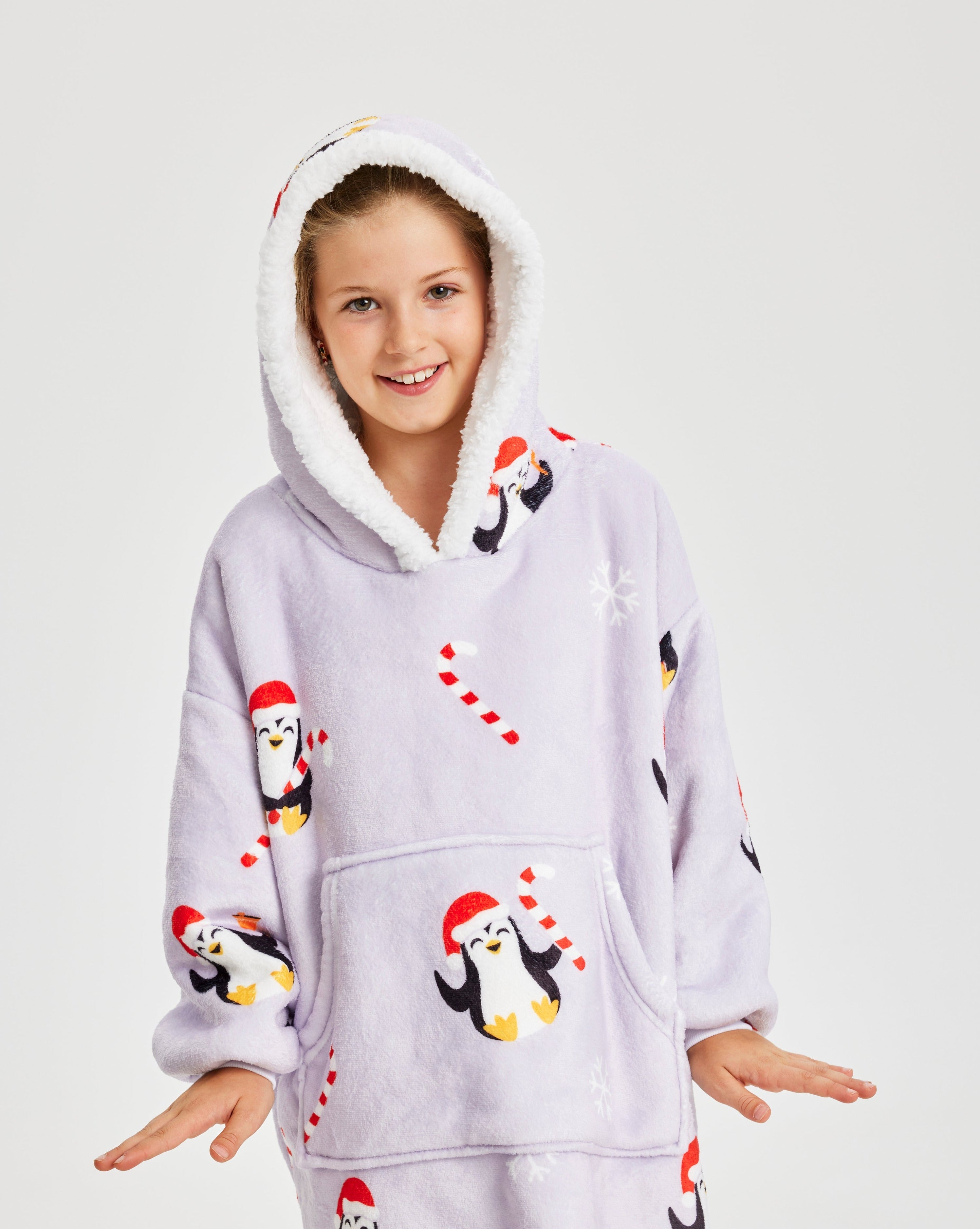 Ein posierendes Kind, das einen helllila Weihnachtskapuzenpulli mit Pinguinen darauf trägt.
